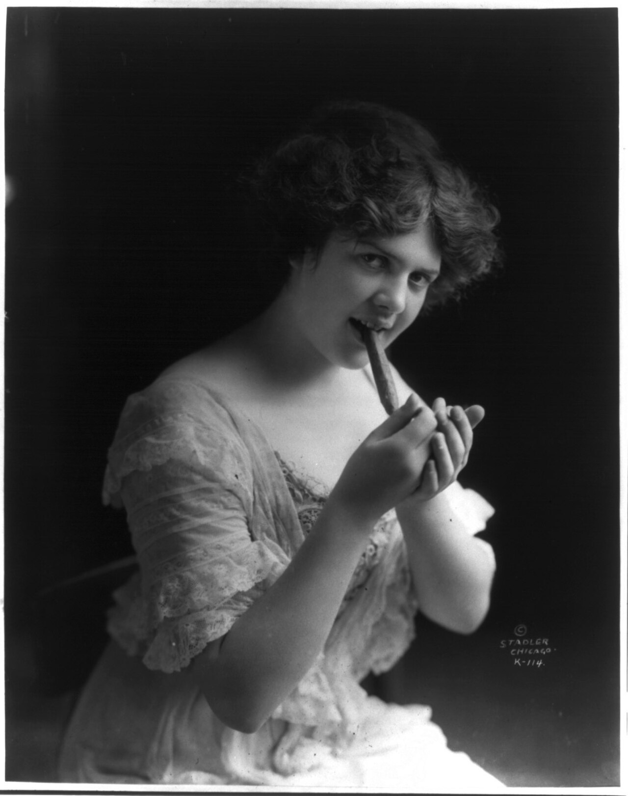 A young woman lighting a cigar in a 1913 studio photograph